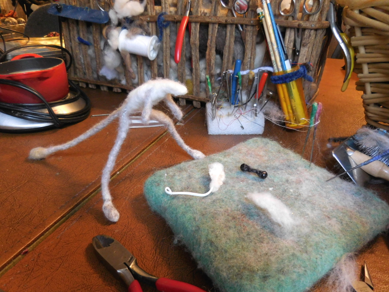 Newish trick: a heavy twist tie covered with waxed wool makes a durable and flexible support for big ears; much better than the thin wire edging used in the past. Meanwhile, right-sized eyes were already on hand. (These days I make several sets at a time whenever the current creature doesn’t like any of the old ones still using the drying comb shown in pic #11 of “Building the Lindsay Raccoon,” with decoupage lacquer to speed up the process. ) Pic #13: Head looking at ears and eyes